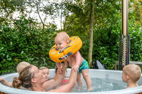 Famiglia si diverte in vasca idromassaggio alla River Cabin + hot tub, Holiday Park Mölke, Paesi Bassi.
