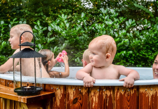 Niños y un adulto disfrutan de una bañera de hidromasaje junto a una cabaña en Holiday Park Mölke, Países Bajos.