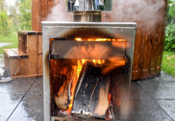 Houtkachel met brandend vuur voor een stomend bubbelbad bij River Cabin in Holiday Park Mölke.