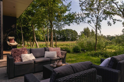 Coin salon extérieur de la River Cabin avec meubles en osier et vue sur le jardin au Holiday Park Mölke, Pays-Bas.