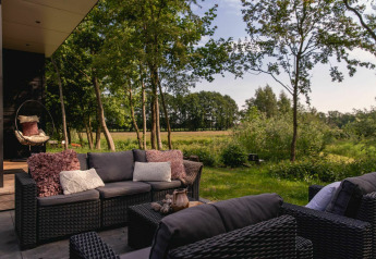Buitenhoek met zithoek aan de River Cabin en zicht op de tuin in Holiday Park Mölke, Nederland.
