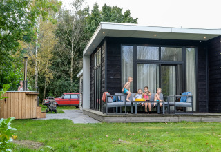 Bambini che giocano e siedono sulla terrazza del River Cabin con hot tub a Holiday Park Mölke, Paesi Bassi.