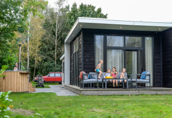 Børn leger og sidder på terrassen ved River Cabin med udendørs badetønde hos Holiday Park Mölke i Holland.