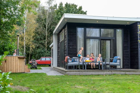 Children playing and sitting on the terrace of River Cabin with hot tub at Holiday Park Mölke, Netherlands.
