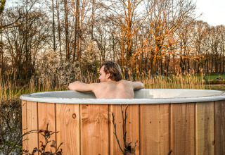 Persoon ontspant in een buiten hottub bij River Cabin, Holiday Park Mölke, Nederland, omringd door natuur.