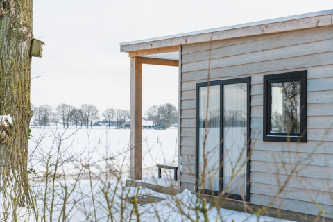 Blick auf das River Lodge Tiny House mit Holzverkleidung im verschneiten Holiday Park Mölke, Niederlande.