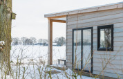 View of the River Lodge tiny house with wood siding and snowy landscape at Holiday Park Mölke, Netherlands.