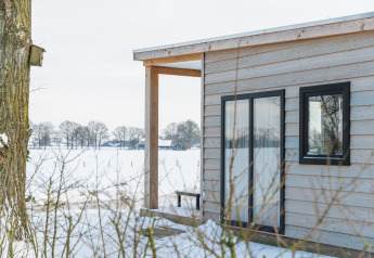 Uitzicht op de River Lodge tiny house met houten bekleding en sneeuw bij Holiday Park Mölke, Nederland.