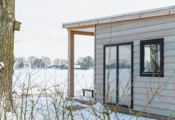 Vista della tiny house River Lodge con rivestimento in legno e neve all’Holiday Park Mölke, Paesi Bassi.