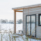 Vue du tiny house River Lodge avec bardage bois et paysage neigeux au Holiday Park Mölke, Pays-Bas.