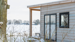 Vista della tiny house River Lodge con rivestimento in legno e neve all’Holiday Park Mölke, Paesi Bassi.