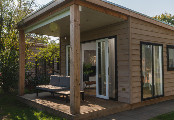 Moderne glampinghut met houten afwerking, overdekt terras en zitbank in een groene, natuurlijke omgeving.