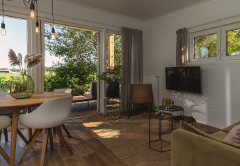 Lichte, moderne glamping woonkamer met eetgedeelte, stoelen en grote ramen met uitzicht op het groen.