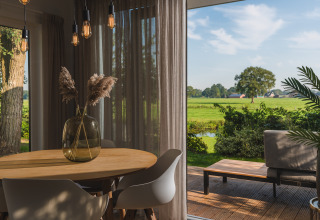 Gezellige eethoek in een glampingverblijf met terras en uitzicht op een groen, landelijk landschap.