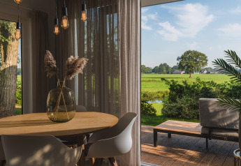 Gezellige eethoek in een glampingverblijf met terras en uitzicht op een groen, landelijk landschap.