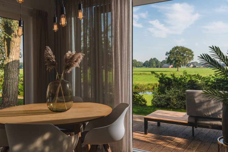 Acogedor comedor luminoso en alojamiento glamping con terraza y vistas a un paisaje verde exterior.