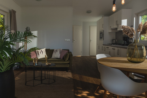 Alloggio glamping moderno con zona living accogliente, cucina attrezzata, tavolo da pranzo e luce naturale.