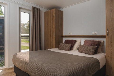 Bedroom inside a glamping accommodation with a double bed, brown pillows, wooden closets, and large window.