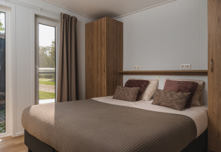 Bedroom inside a glamping accommodation with a double bed, brown pillows, wooden closets, and large window.