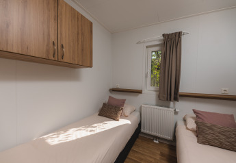 Moderne glampingkamer met twee aparte bedden, houten kasten, venster, radiator en zachte kussens.
