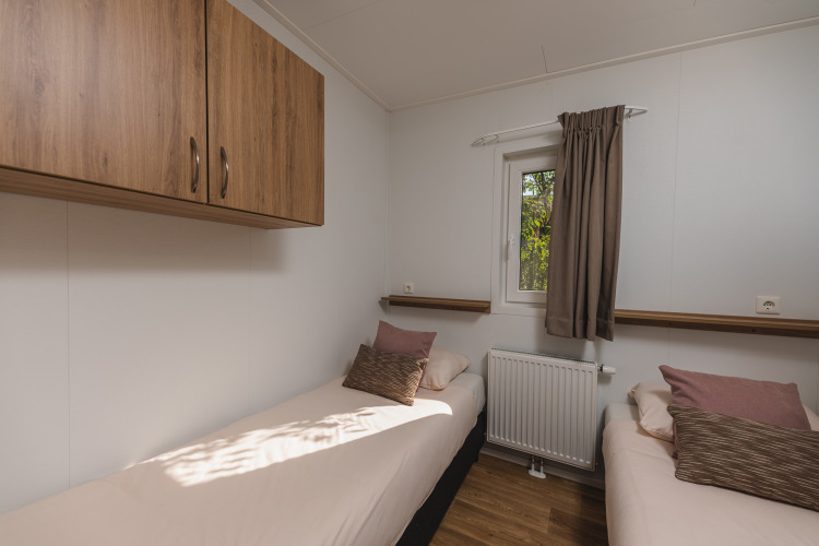 Habitación glamping moderna con dos camas individuales, armarios de madera, ventana y cojines cómodos.