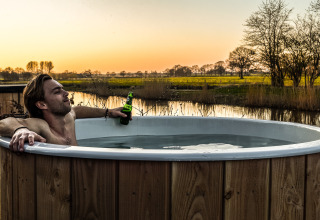 Uomo che si rilassa in una vasca idromassaggio all'aperto con birra al tramonto al Holiday Park Mölke, Paesi Bassi.