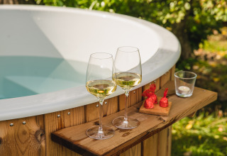 Deux verres de vin blanc et des chocolats à côté d’un jacuzzi extérieur à River lodge + hot tub, Holiday Park Mölke.