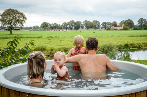 Familie nyder et udendørs spabad med udsigt over grønne marker ved River lodge i Holiday Park Mölke.