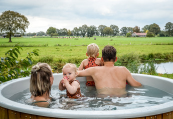 Gezin in de jacuzzi met uitzicht op groene velden bij River lodge, Holiday Park Mölke in Nederland.