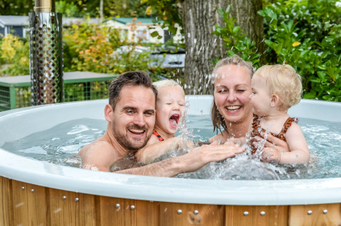 Gezin ontspant lachend in de hot tub bij River Lodge Tiny House, Holiday Park Mölke, Nederland.