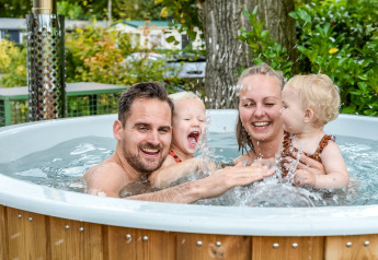 Gezin ontspant lachend in de hot tub bij River Lodge Tiny House, Holiday Park Mölke, Nederland.