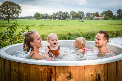 Famiglia si rilassa nella vasca idromassaggio con vista campagna al River lodge, Holiday Park Mölke.