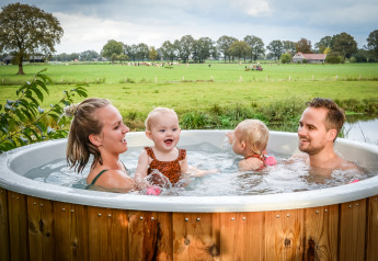 Gezin genietend van een hottub met uitzicht op velden bij River lodge, Holiday Park Mölke.