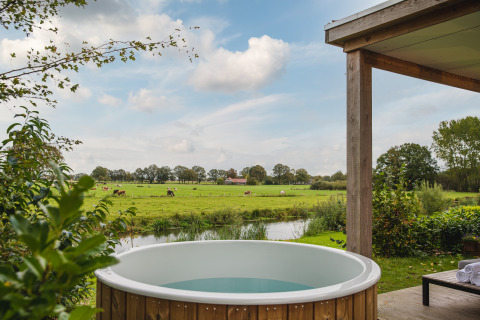 Uitzicht vanuit River lodge met buitenjacuzzi bij Holiday Park Mölke, groene velden en koeien te zien.