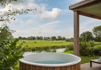 Uitzicht vanuit River lodge met buitenjacuzzi bij Holiday Park Mölke, groene velden en koeien te zien.