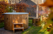 Wood-fired hot tub next to Reggehooiberg tiny house at Holiday Park Mölke, Netherlands, in autumn foliage.
