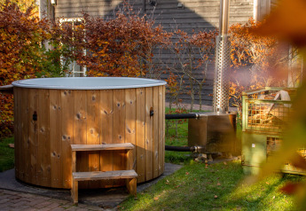 Houten hot tub naast het Reggehooiberg tiny house op Vakantiepark Mölke, Nederland, omgeven door herfstbladeren.