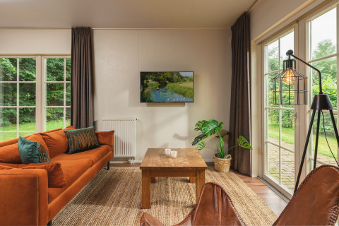 Gezellige woonkamer in een tiny house met oranje bank, grote ramen en tuinzicht bij Holiday Park Mölke.