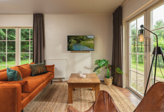Cozy living room in a tiny house with orange sofa, large windows and garden view at Holiday Park Mölke.