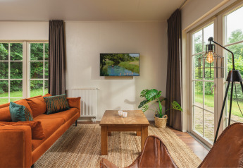 Gezellige woonkamer in een tiny house met oranje bank, grote ramen en tuinzicht bij Holiday Park Mölke.
