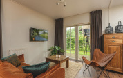 Cozy glamping accommodation lounge with orange sofa, butterfly chair, and garden view through glass doors.
