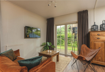 Knusse glamping woonkamer met oranje bank, vlinderstoel, houten meubels en uitzicht op de groene tuin.