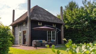 Charming group lodge Reggehooiberg with thatched roof, outdoor patio, and large backyard in lush greenery.