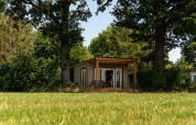 Tiny wooden cabin with terrace set among trees at Holiday Park Mölke in the Netherlands, sunny day.