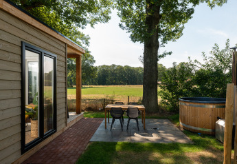 Gezellig terras met houten tafel, stoelen en hottub naast een tiny house in het Nederlandse platteland.