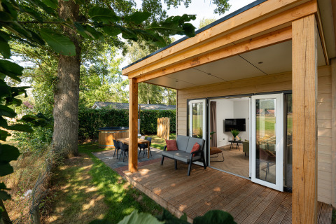 Træbeklædt tiny house med overdækket terrasse, udendørs spiseområde og vildmarksbad i naturskønne Holland.