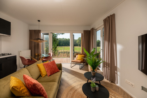 Sala de estar de una tiny house en Holiday Park Mölke con grandes ventanales y vista a los campos verdes.