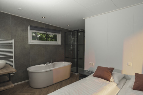 Habitación glamping moderna con bañera independiente, ducha de vidrio, cama cómoda y ventana amplia.