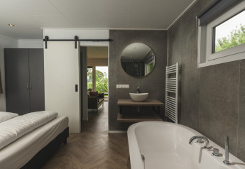 Moderne glamping accommodatie met slaapkamer, open badkamer, vrijstaand bad en uitzicht op groen.