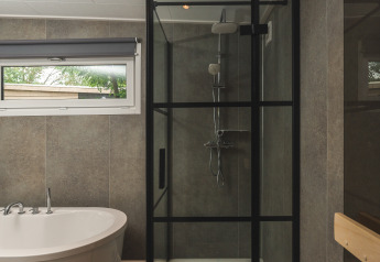 Moderne badkamer in glamping met vrijstaand bad en glazen douche met zwarte omlijsting en houtvloer